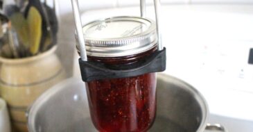 lowering a mason jar into a water bath canner
