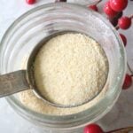 homemade garlic powder in a copper tablespoon over a glass mason jar. Red berries in the background