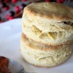 2 homemade biscuits on a white plate with a spoonful of jam beside it.
