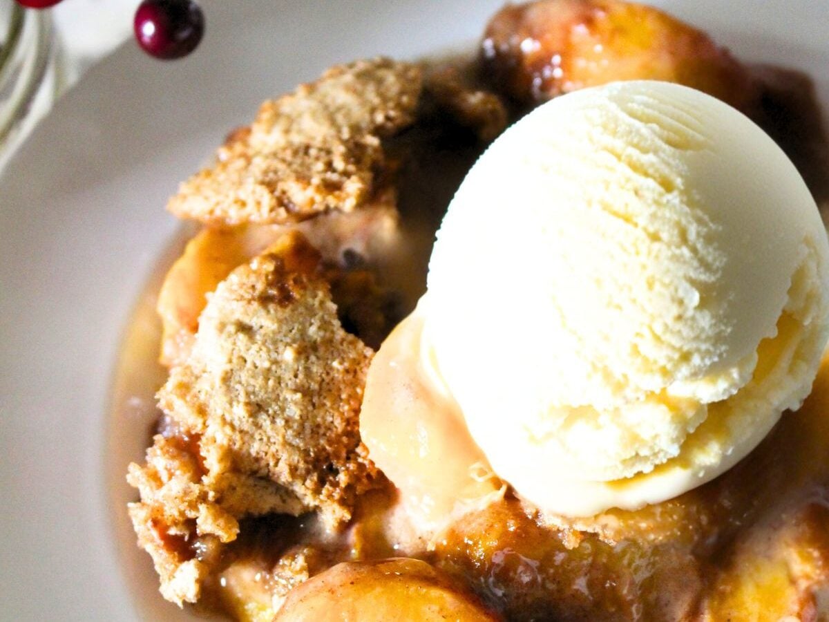 a bowl of homemade peach crumble topped with vanilla ice cream