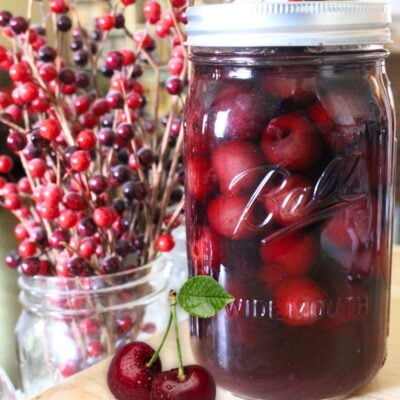 a quart mason jar of home canned cherries with 2 fresh cherries beside the jar