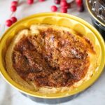 A close up of a finished mini pecan pie with a stack of pecan pies in the background.