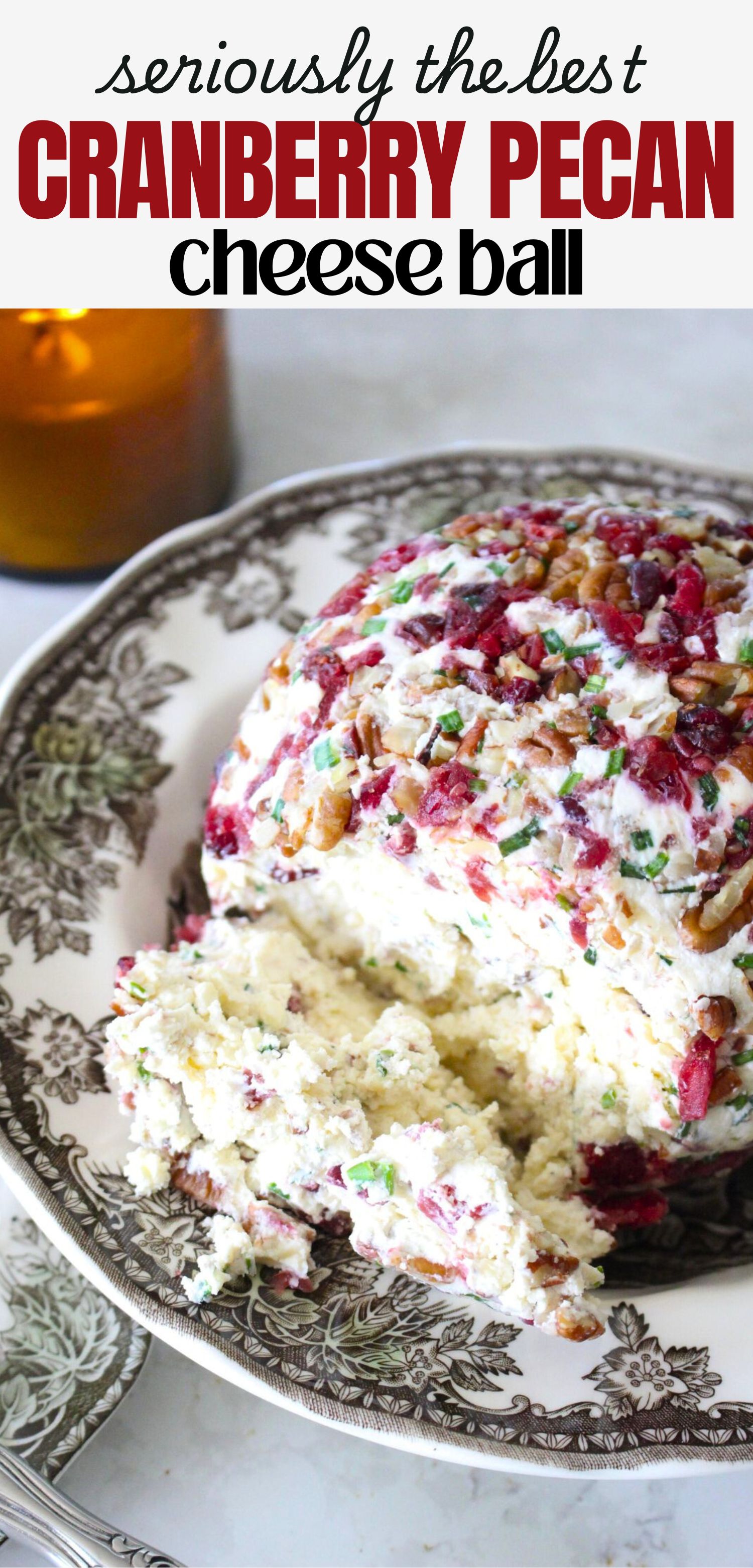 Close up of a finished cranberry pecan cheese ball in a vintage bowl, a lit candle in the background. A text overlay reads seriously the best cranberry pecan cheese ball.