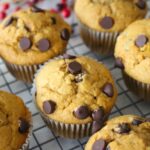 Finished sweet potato muffins topped with chocolate chips on a cooling rack, a jar of red berries in the background.