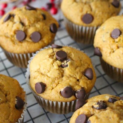 Finished sweet potato muffins topped with chocolate chips on a cooling rack, a jar of red berries in the background.
