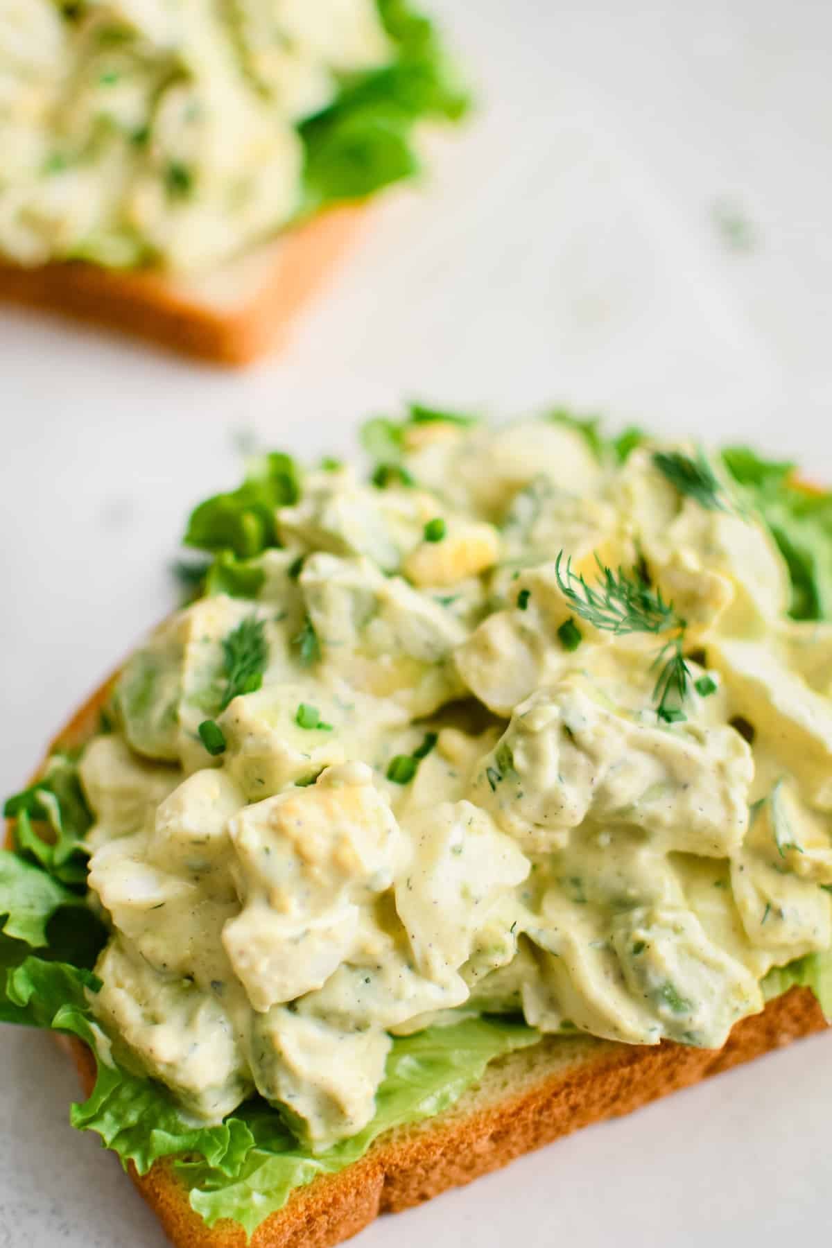 two pieces of bread with lettuce and avocado egg salad piled high