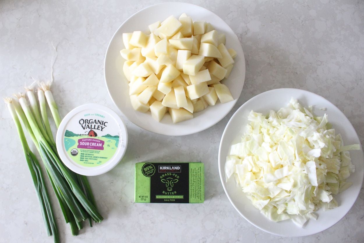 Prepped ingredients for colcannon potatoes, including potatoes, cabbage, butter, green onions, and sour cream.