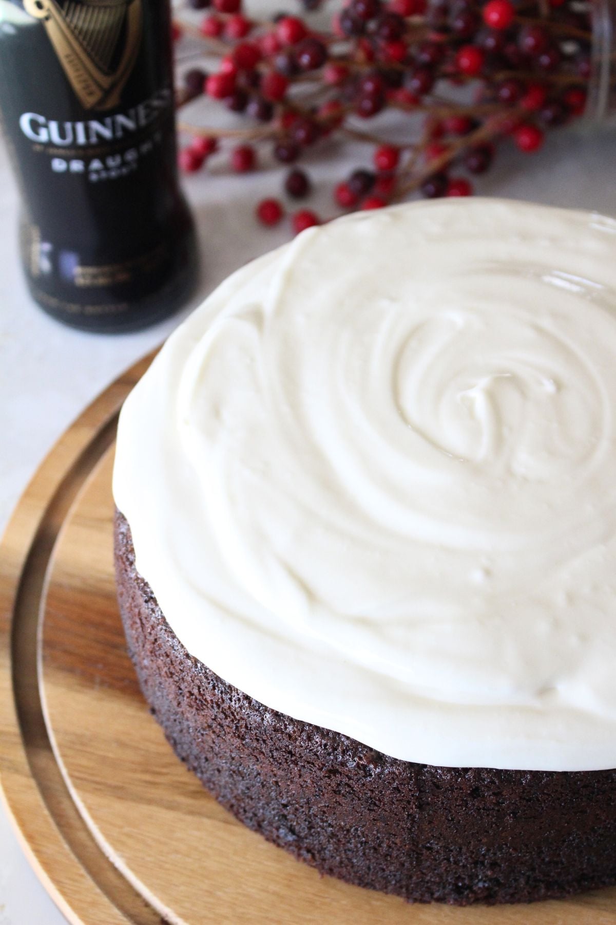 The whole finished Guinness chocolate cake topped with cream cheese frosting and made to look like a pint of guinness beer. A bottle of guinness in the background. 