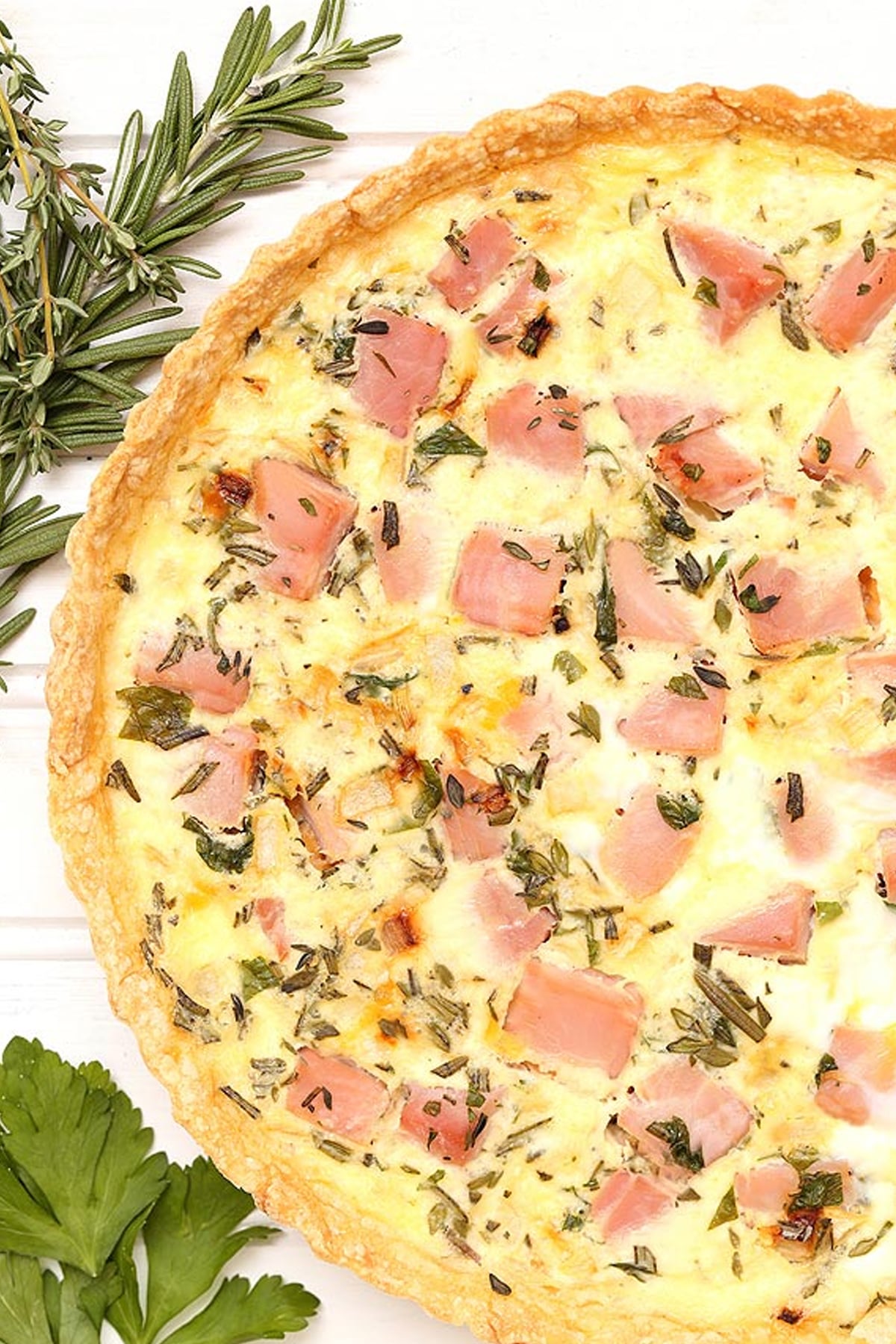 top down view of a Ham and Herb Quiche surrounded by bunches of herbs