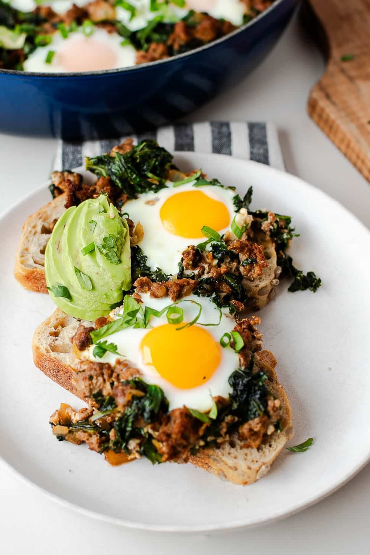 a white plate with two pieces of homemade bread covered in One Pan Chorizo Baked Eggs Recipe with Veggies and avocado slices