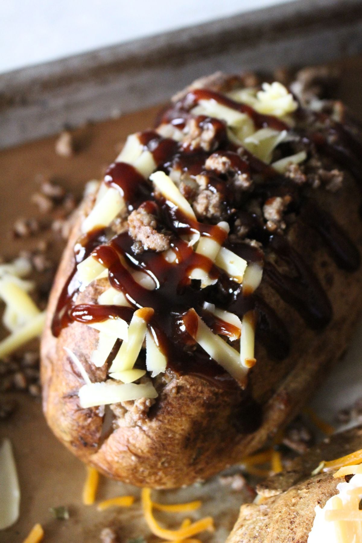 Finished oven baked potato topped with BBQ meat, cheese, sour cream, and BBQ sauce
