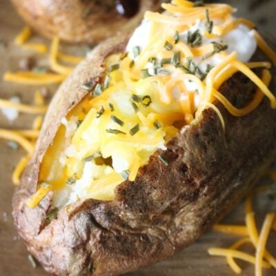Finished homemade baked potato in oven finished with butter, cheese, sour cream, and chives.