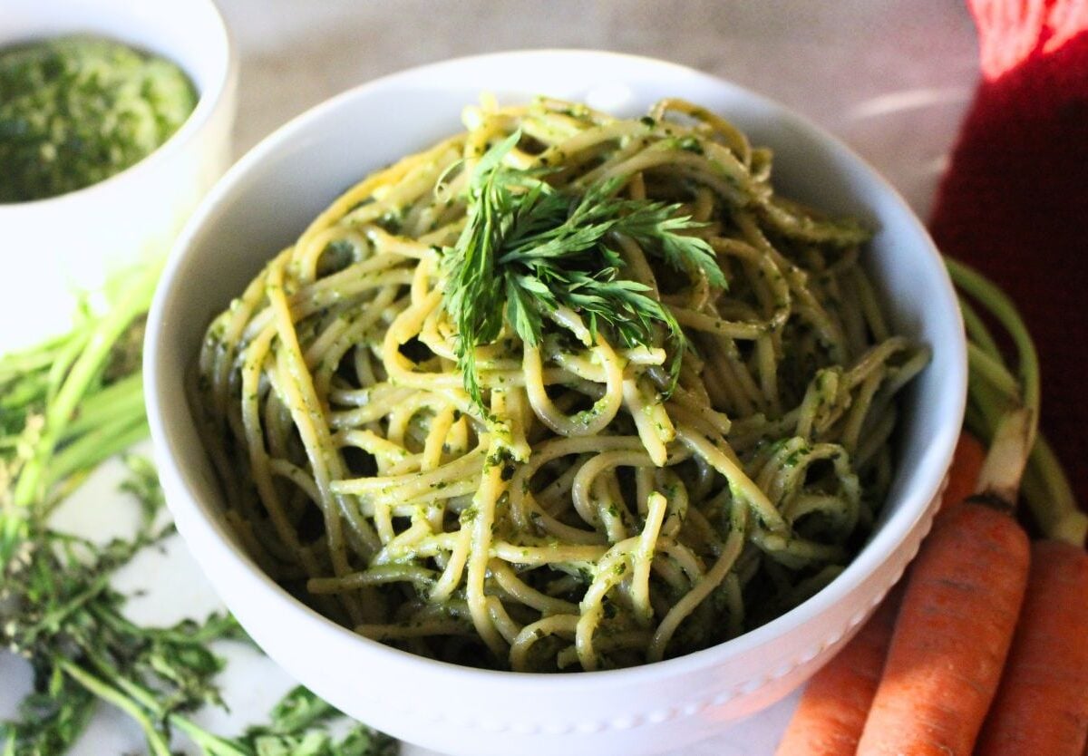 Finished carrot top pesto tossed over pasta in a white bowl ready to serve