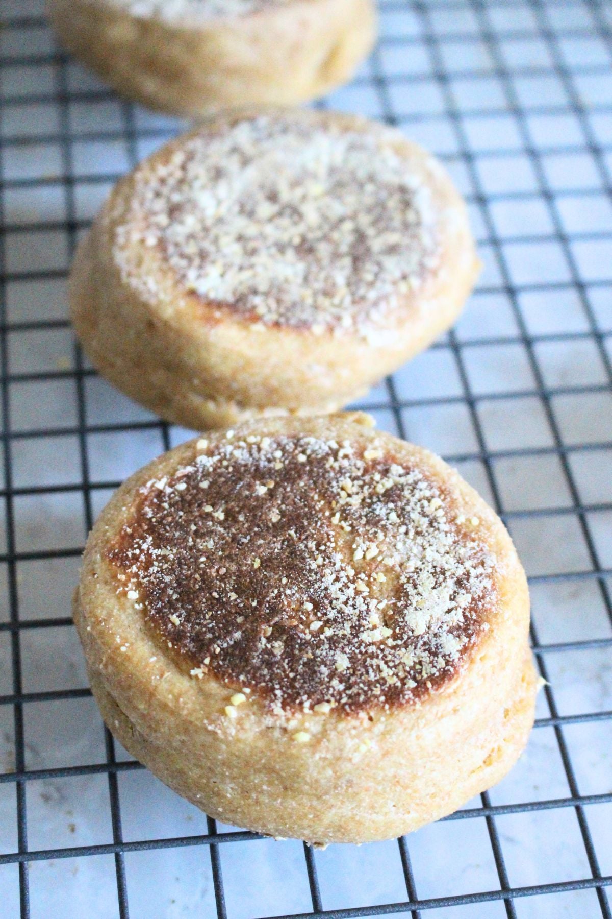 3 homemade English Muffins cooling on a baking rack.