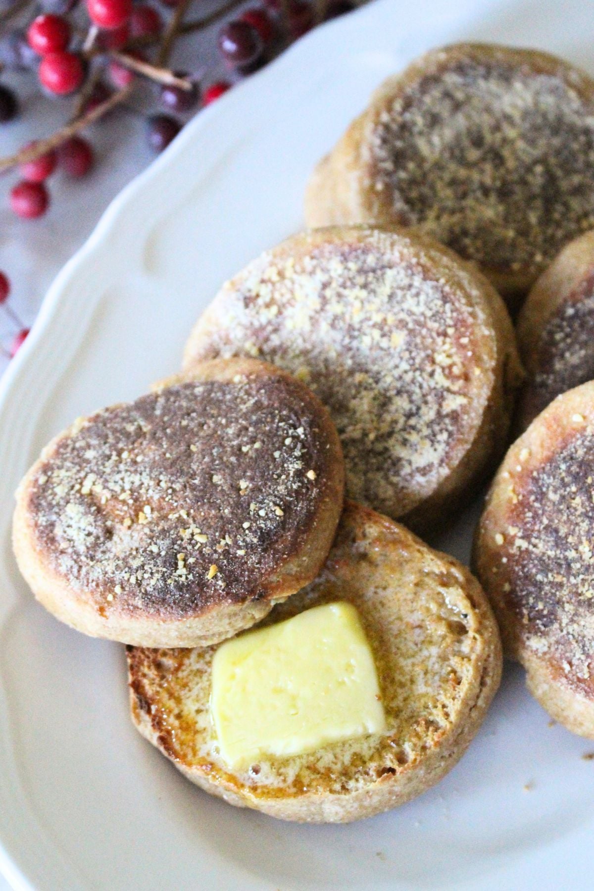 Finished homemade english muffins on a plate, one is cut open and toasted with melting butter on the middle.