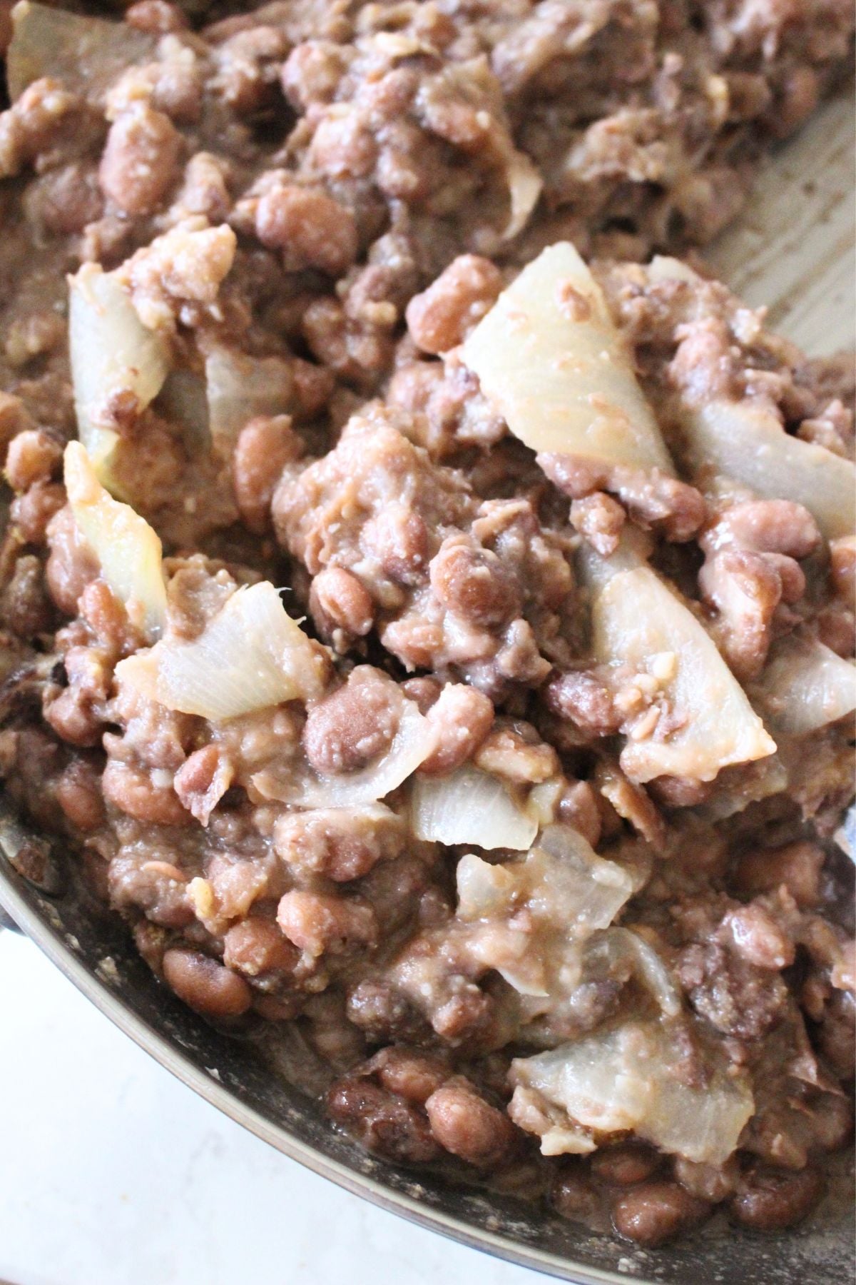 pinto beans and onions in a skillet being fried and mashed for homemade refried beans.