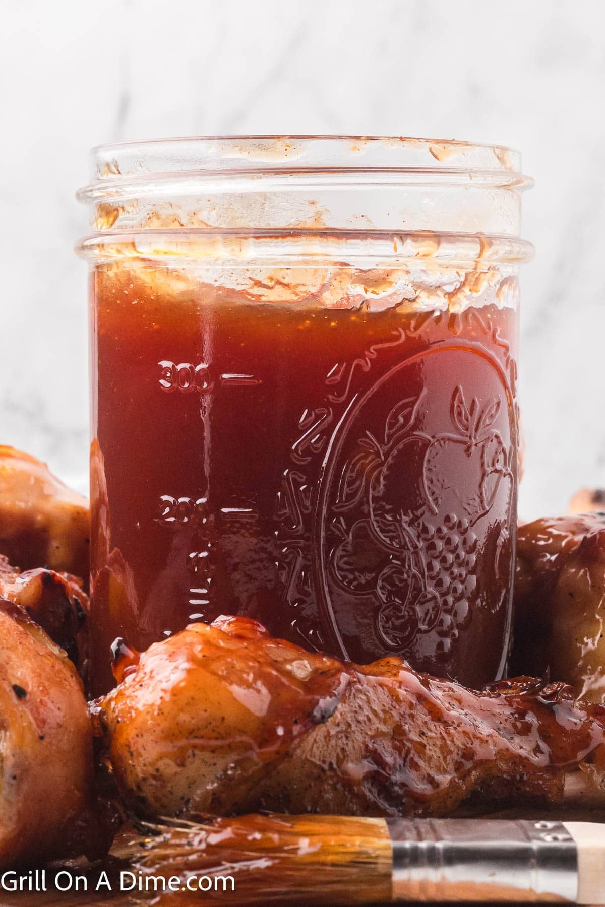 Peach BBQ Sauce in a mason jar with a basting brush and chicken wings beside it