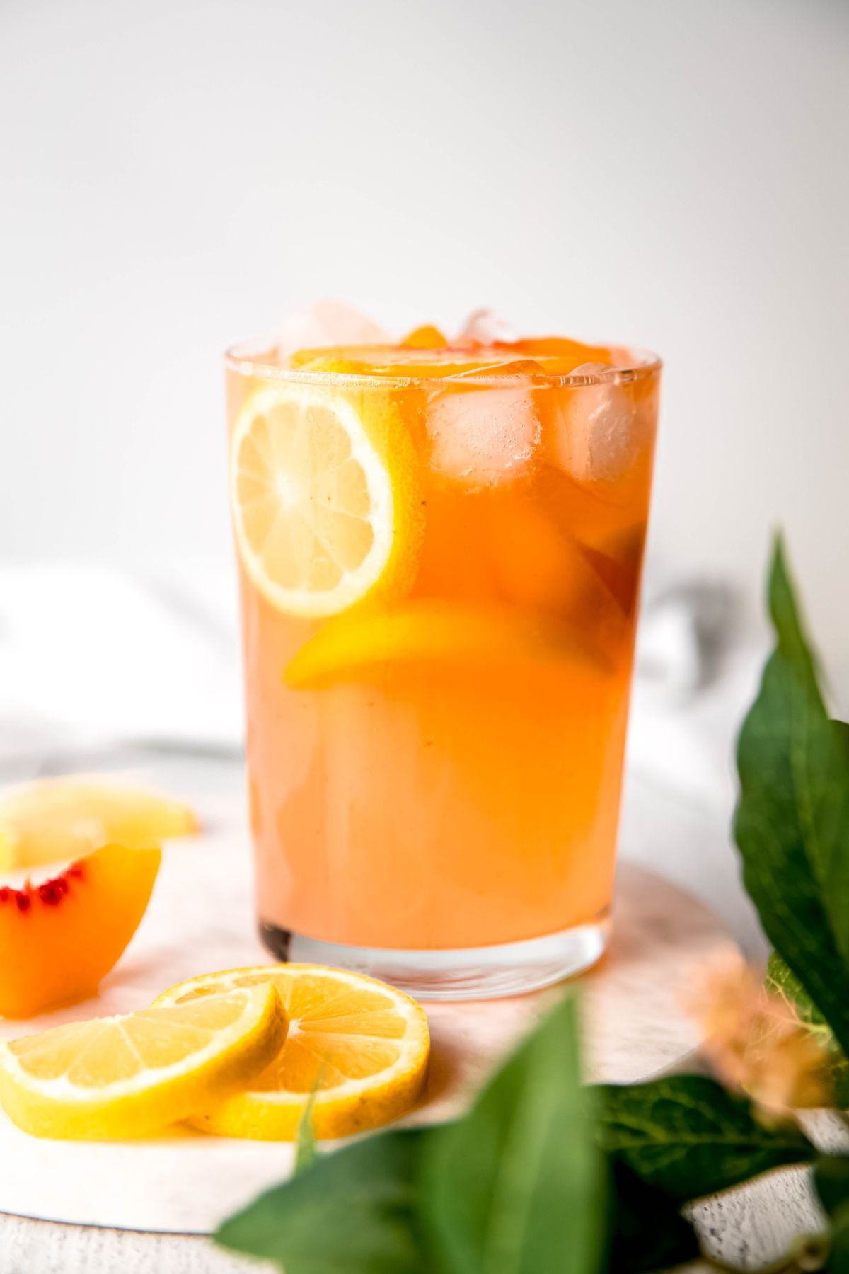 Peach Lemonade in a pint glass with mint and fresh cut peaches and lemons around the glass