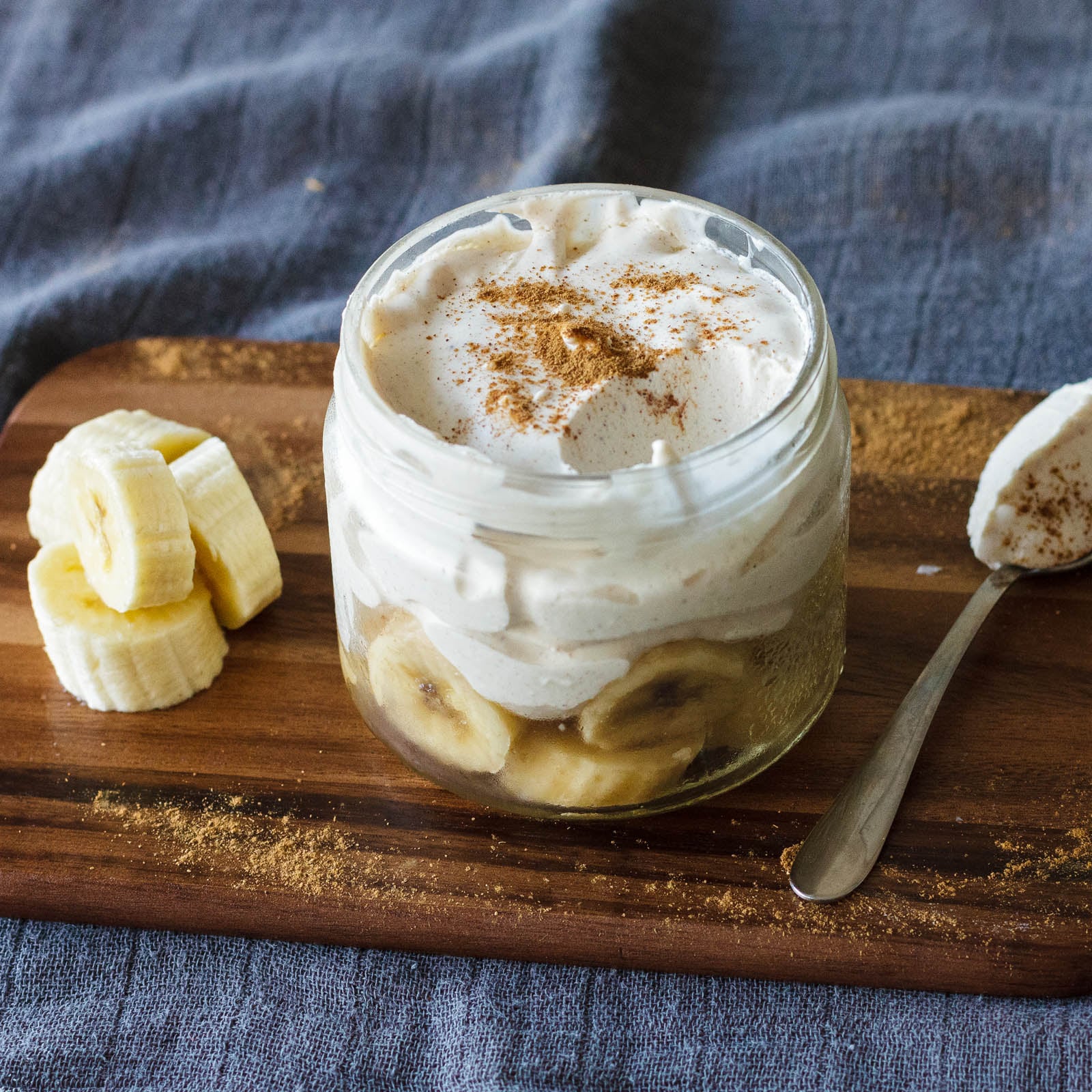 Banana Cinnamon Whipped Cream Dessert in a small glass jar with banana slices next to it