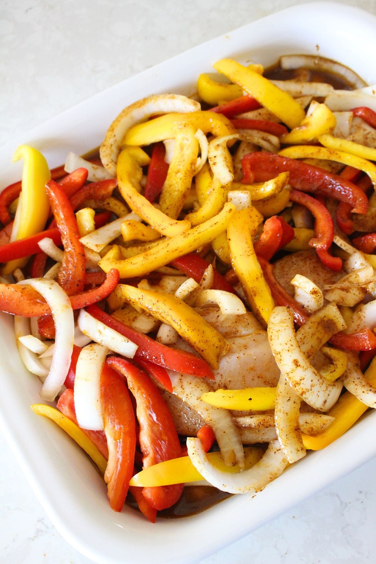 chicken, onions, and peppers in a baking tray covered in marinade and ready to rest.