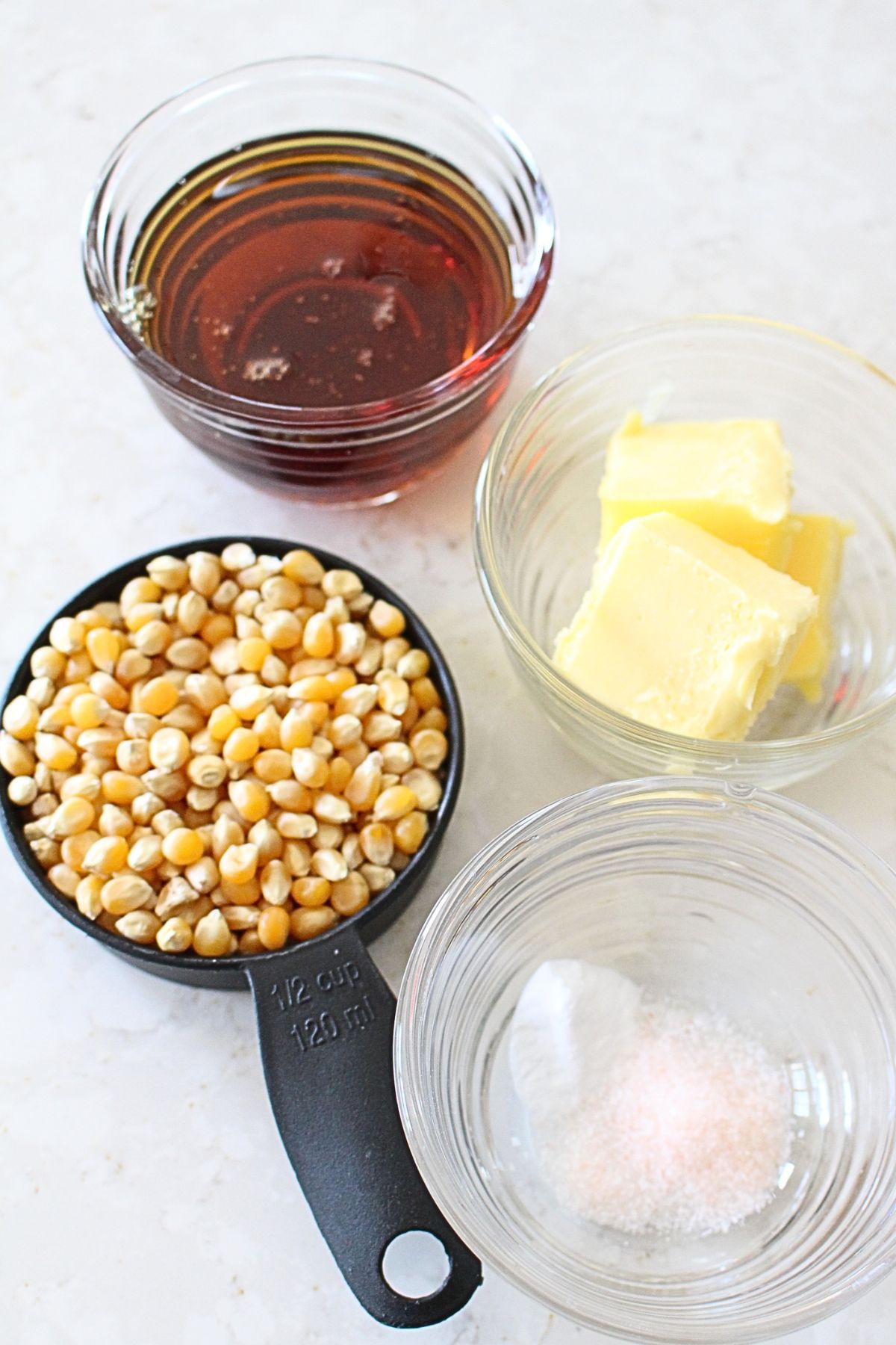 the ingredients for caramel popcorn, including maple syrup, butter, popcorn, salt, and baking soda.
