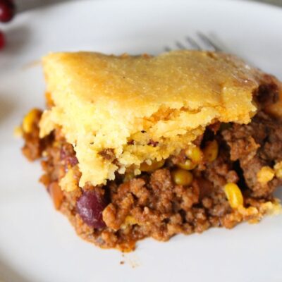 Finished serving of cornbread casserole, cowboy casserole in a white plate with the baking dish remainder in the background.