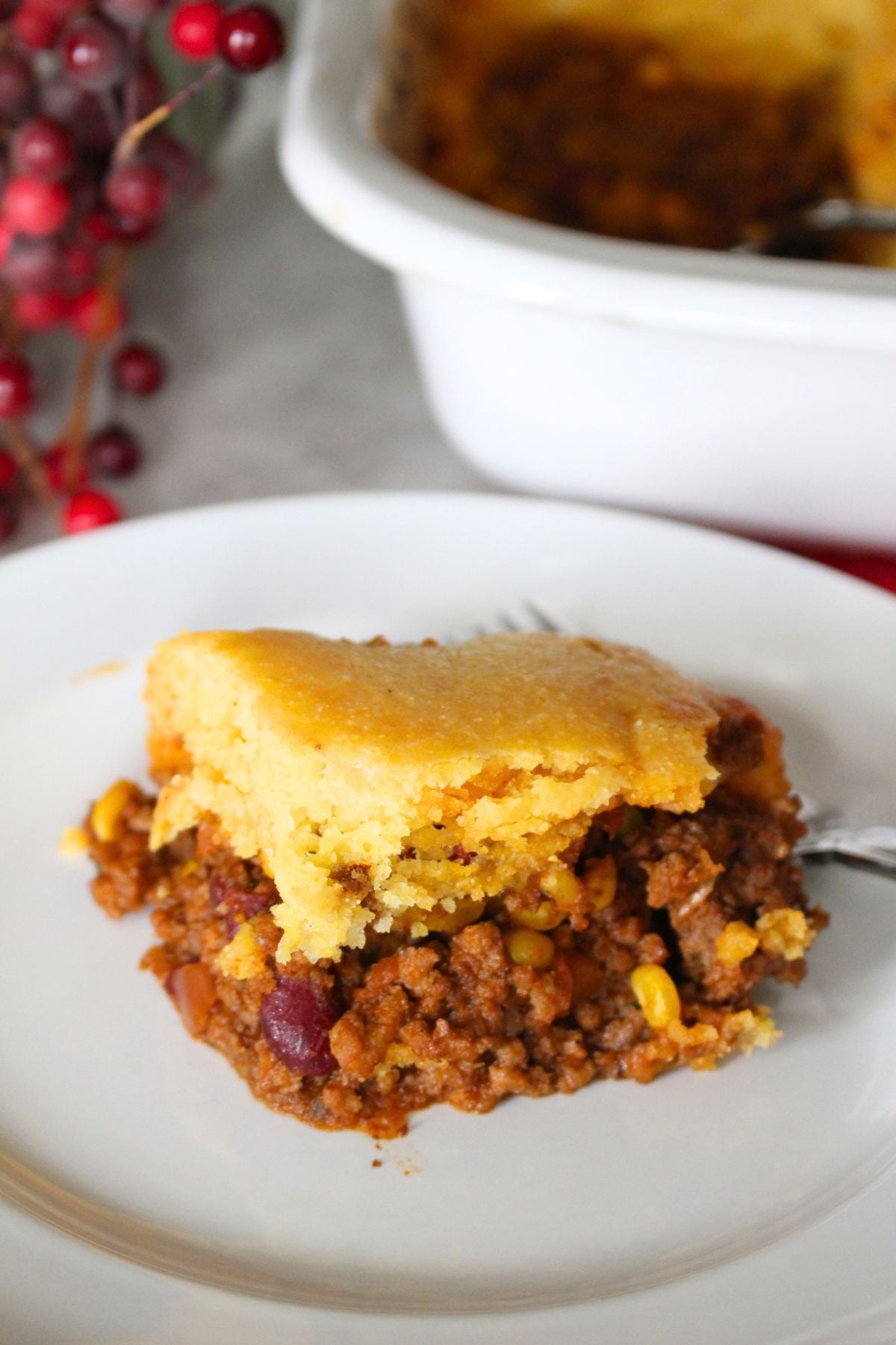 Finished serving of cornbread casserole, cowboy casserole in a white plate with the baking dish remainder in the background.