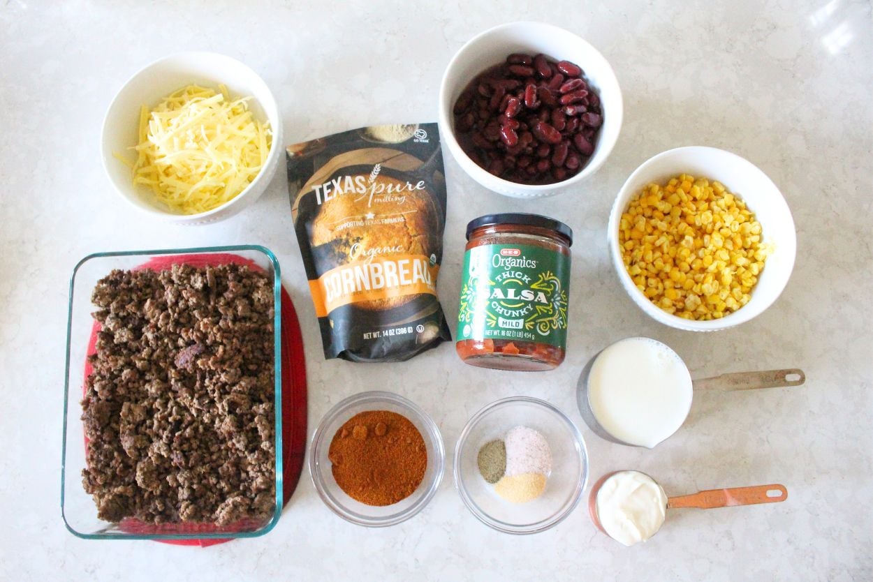 All of the ingredients needed for cornbread cowboy casserole laid out in containers on a white kitchen counter.