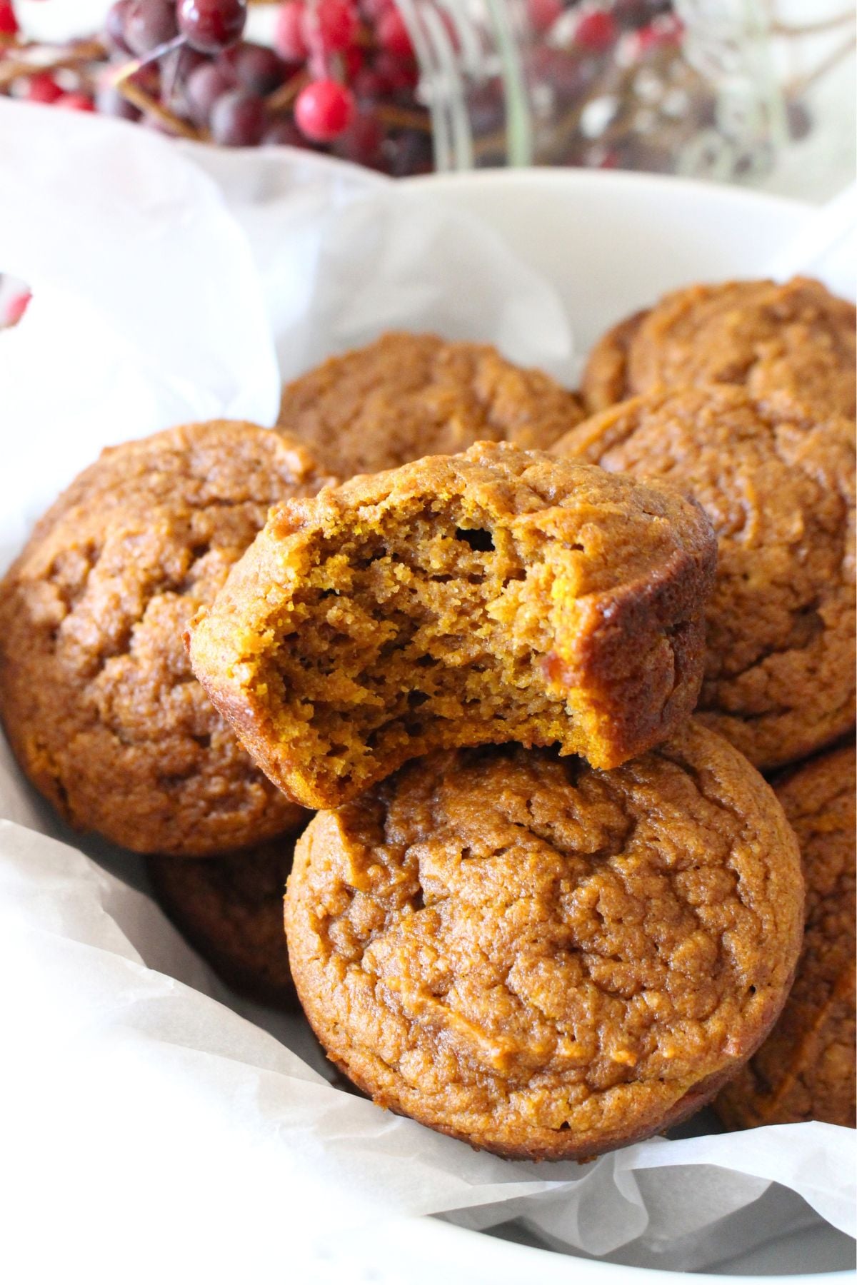 a finished pumpkin muffin with a bit taken out so you can see the crumb. It sits on top of a pile of other finished pumpkin muffins