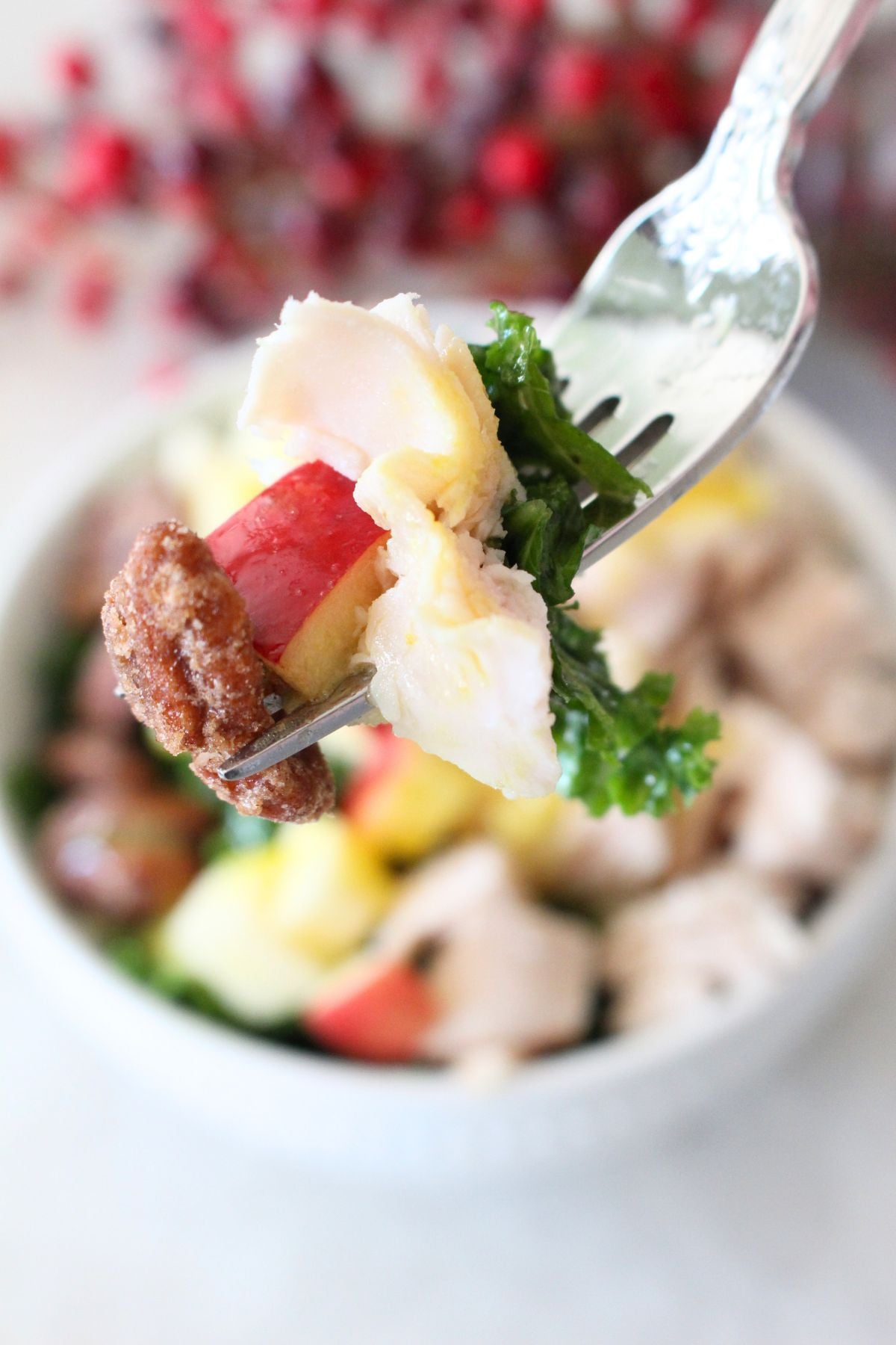 forkful of Finished turkey apple pecan kale salad, a white bowlful is in the background